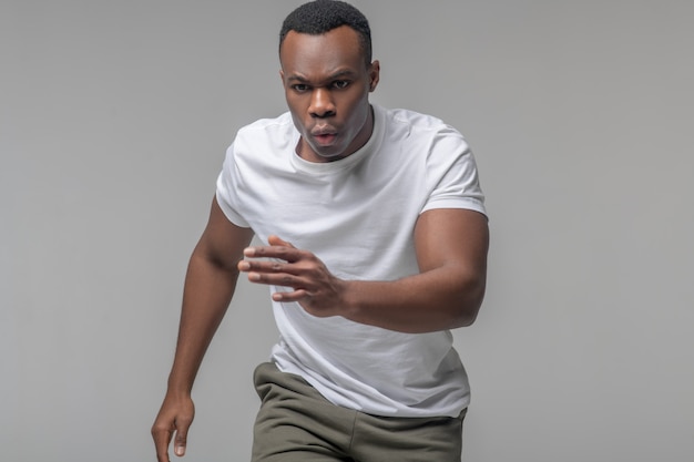 Sportiviteit. Energieke gefocuste jonge zwarte man in een witte t-shirt met ademhaling correct zwaaiend met zijn armen
