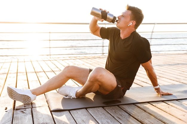 Sportman buiten op het strand drinkwater.