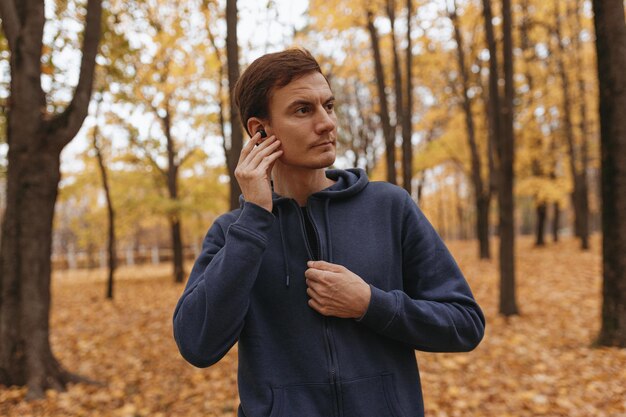 Sportman die naar muziek luistert in draadloze oortelefoons tijdens de training in het herfstpark