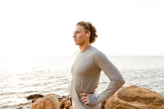 Sportman die op het strand staat en muziek luistert met oortelefoons.