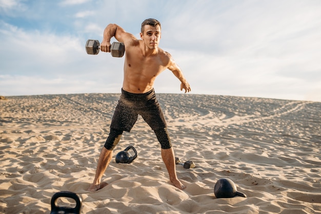 Sportman doet oefeningen met gewichten in de woestijn op zonnige dag. Sterke motivatie in sport, krachttraining buitenshuis