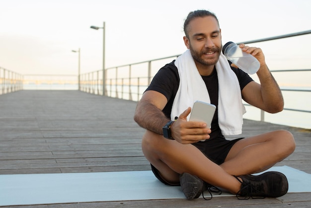 Sportman drinkt water en gebruikt zijn smartphone na een training in de buitenlucht