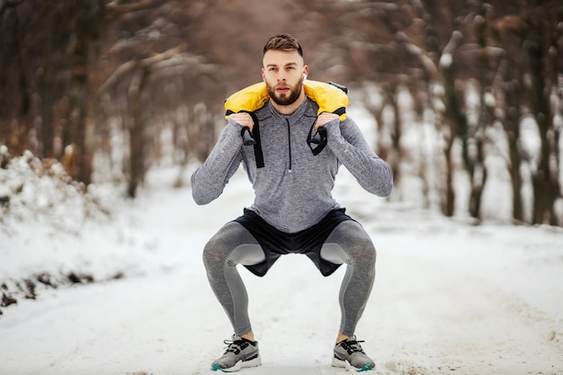 Sportman hurkt en houdt gewichten in de natuur op besneeuwde winterdag. Bodybuilding, gezonde gewoontes, winterfitness