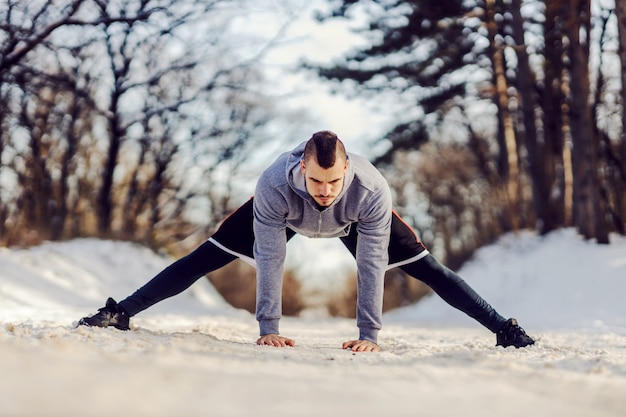 Sportman in vorm die op een besneeuwd pad in de natuur staat en warming-up en rekoefeningen doet. Winterfitness, flexibiliteit, gezond leven