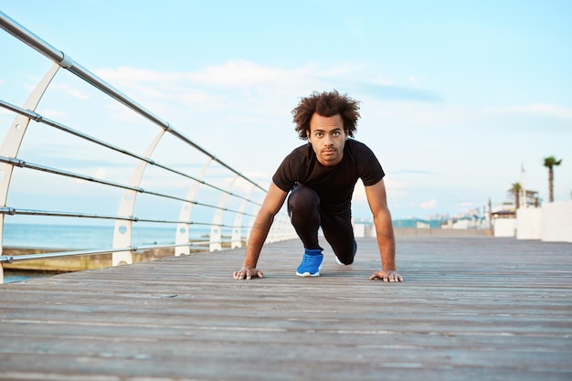 Sportman met donkere huid en borstelig kapsel die zich uitstrekt voordat hij 's ochtends buiten gaat hardlopen