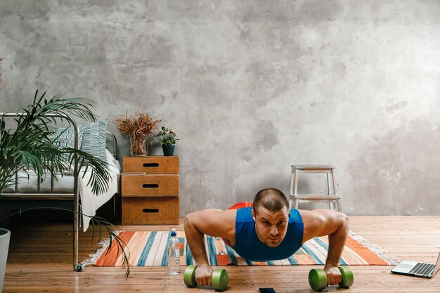 Foto sportman met zwart haar doet push-ups met dumbbells en kijkt naar een film kijken naar een workout online