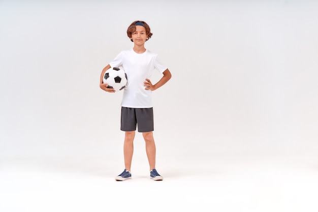 Sports activities fulllength shot of a happy teenage boy holding soccer ball looking at camera and