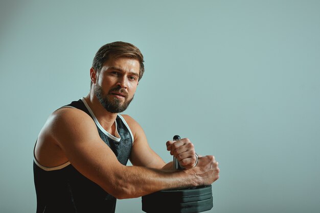 Sports, activity, health and fitness concept. Fit young male athlete standing with barbell against grey wall background with copy space for your content