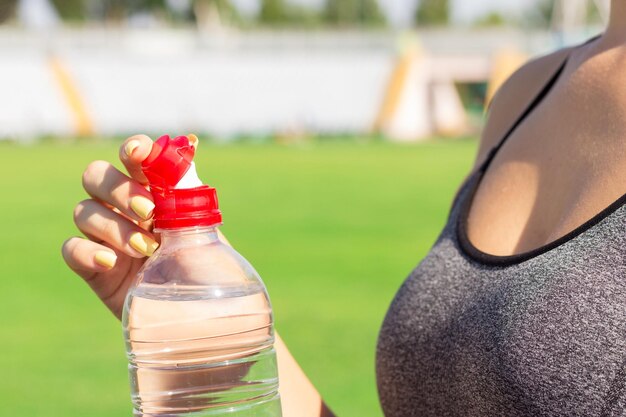 スポーツと健康的なコンセプトの女性アスリートは、スタジアムでのトレーニング後に水を飲むためにペットボトルを開いています