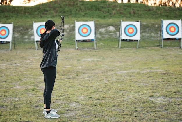 Foto tiro con l'arco sportivo e allenamento con arco e frecce per la sfida dell'atleta da competizione con l'arciere o la pratica sul campo delle ragazze obiettivo di tiro e donna competitiva concentrarsi su mira di precisione o mockup all'aperto