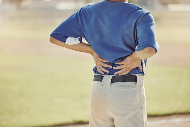Photo sports baseball injury and man with back pain emergency or muscle strain during game competition or fitness match softball player field pitch or back view of athlete with hurt spine or backache