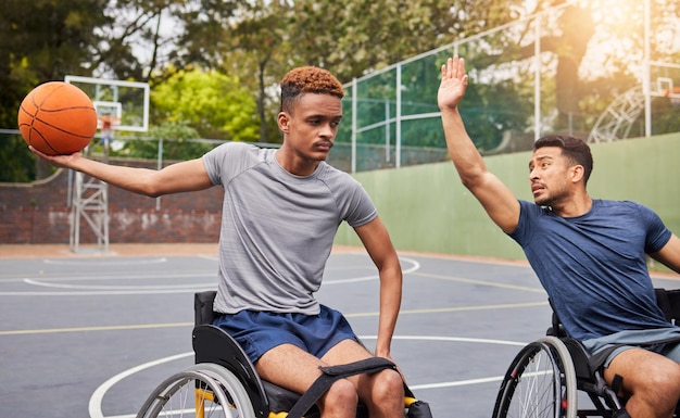 スポーツバスケットボールと屋外コートでのトレーニング運動とトレーニングのための車椅子の男性フィットネスチームと競技練習やゲームでボール遊びをする障害のある男性