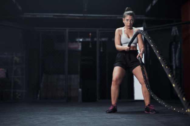 Sports battle ropes and woman at the gym doing strength cardio and challenge exercise with space Fitness energy and strong female athlete doing health workout or training with equipment for power