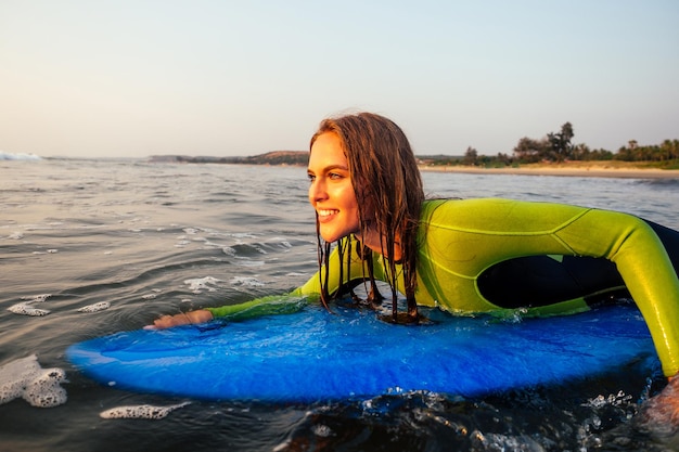 Sports beautiful woman in a diving suit lying on a surfboard\
waiting for a big wave .surf girl in a wetsuit surfing in the ocean\
at sunset.wet hair, happiness and freedom beach holiday