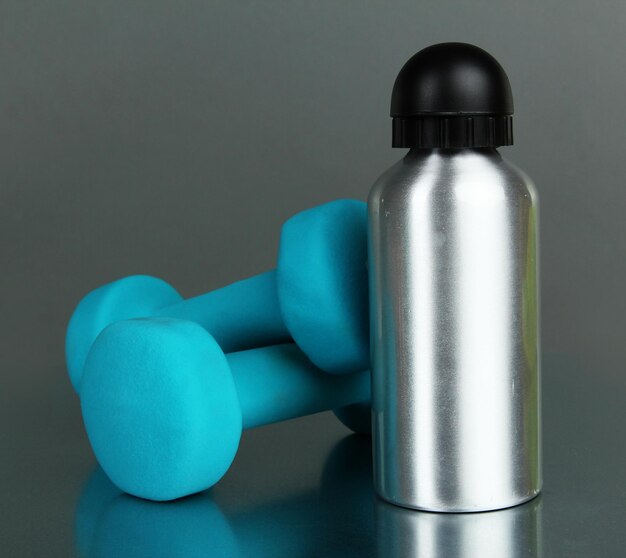 Sports bottle and dumbbells on grey background