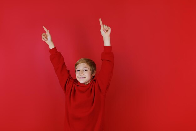 赤いスーツを着たスポーツ少年が手を上に伸ばし、指を上に向ける