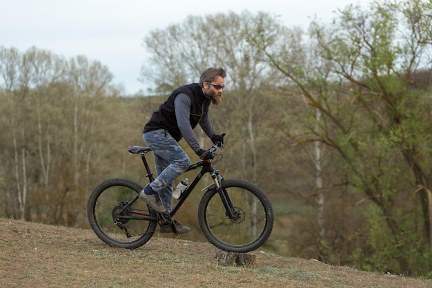 春の緑の丘で現代のマウンテンバイクサイクリストのスポーツ残忍なひげを生やした男