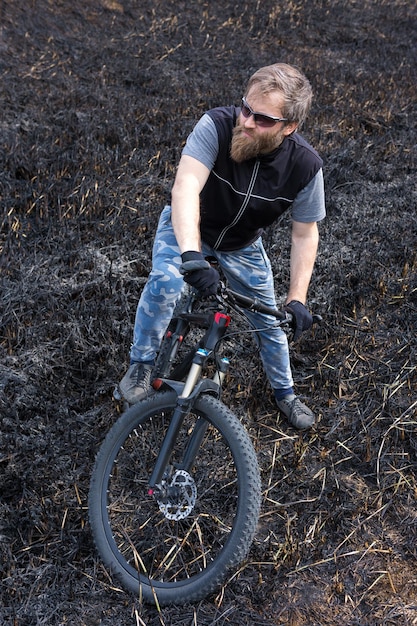 Sports brutal bearded guy on a modern mountain bike Cyclist on the green hills in the spring