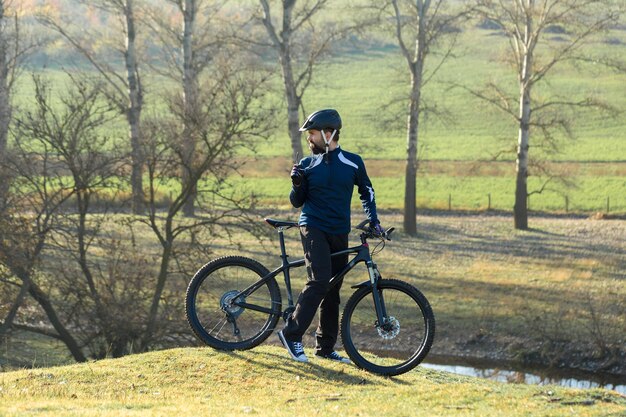 Спортивный брутальный бородатый парень на современном горном велосипеде Велосипедист на зеленых холмах весной