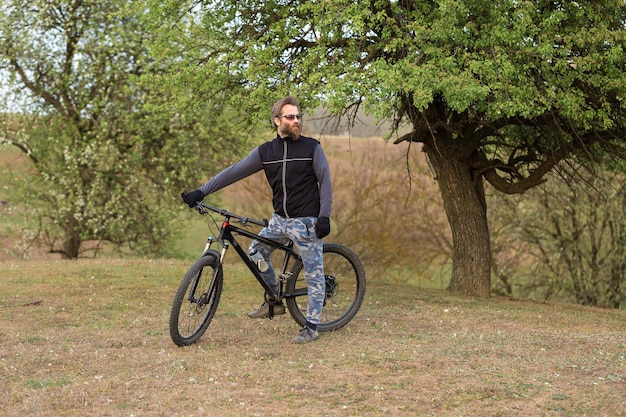 Sports brutal bearded guy on a modern mountain bike Cyclist on the green hills in the spring