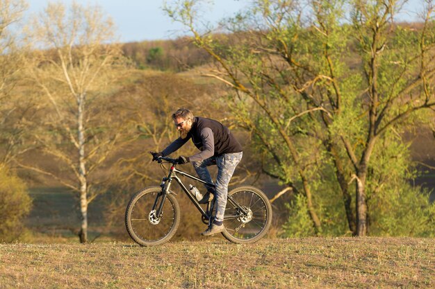 Sports brutal bearded guy on a modern mountain bike cyclist on\
the green hills in the spring