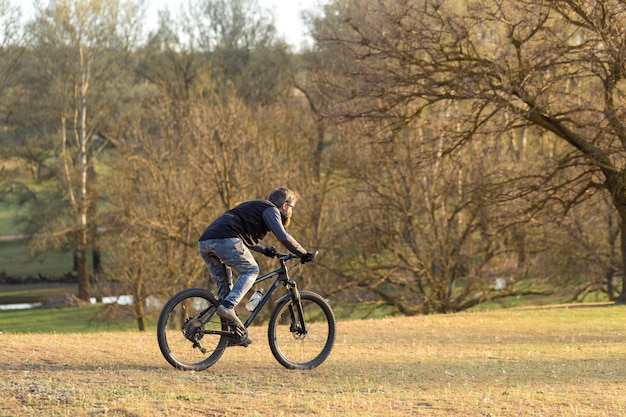 春の緑の丘で現代のマウンテンバイクサイクリストのスポーツ残忍なひげを生やした男