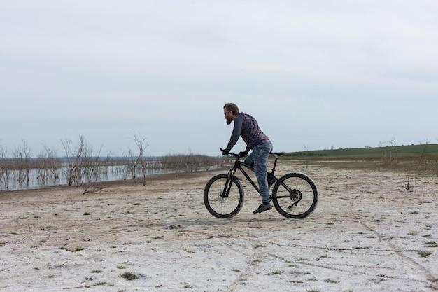 現代のマウンテンバイクでスポーツの残忍なひげを生やした男湖のほとりの塩の人里離れた場所にいるサイクリスト