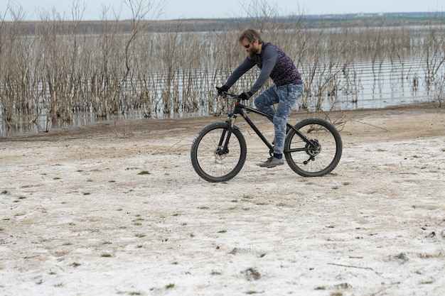 現代のマウンテンバイクでスポーツの残忍なひげを生やした男湖のほとりの塩の人里離れた場所にいるサイクリスト