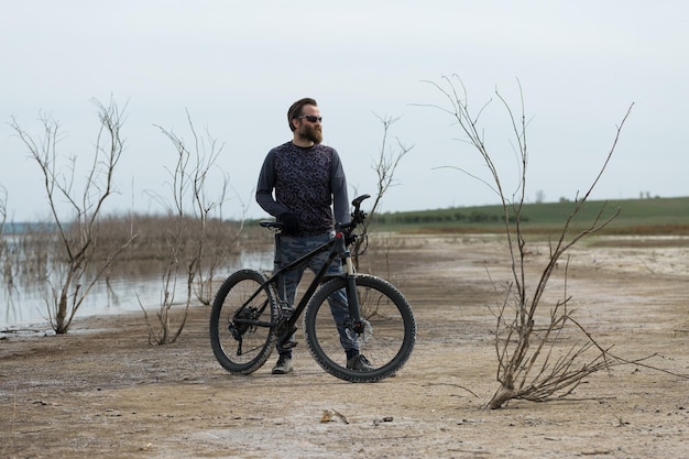 現代のマウンテンバイクでスポーツの残忍なひげを生やした男湖のほとりの塩の人里離れた場所にいるサイクリスト