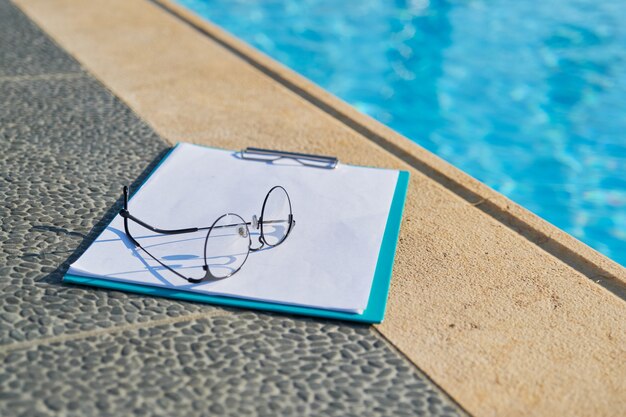 Photo sports concept, active healthy lifestyle, business hotel. nobody, glasses, blank paper, clipboard near outdoor swimming resort pool