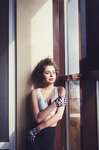 Sports curly woman standing at the window