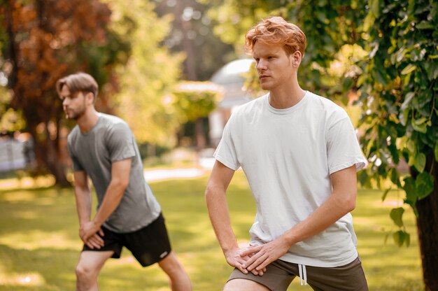 Sports exercise. Two focused athletic guys in sportswear doing exercises vigorously outdoors on warm sunny morning