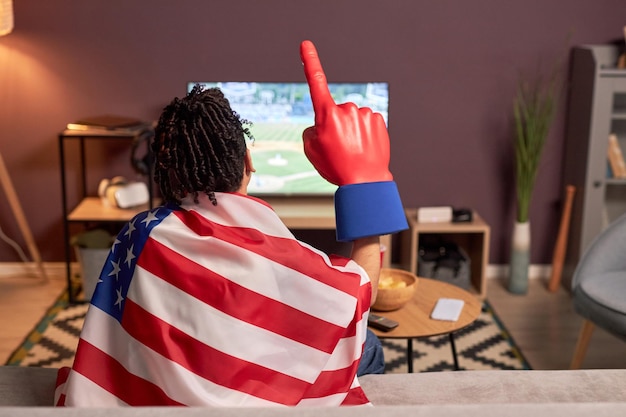 Appassionato di sport che indossa la bandiera mentre guarda la partita di baseball in tv a casa e tifa