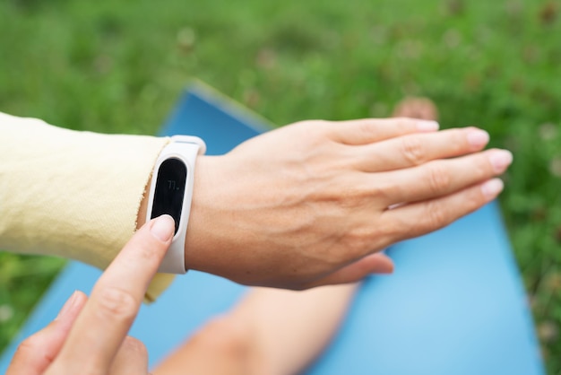 Sports girl doing stretching in nature outdoors the girl looks at her fitness bracelet and checks her breathing during exercise A woman is doing yoga in the park sitting on the grass on a yoga mat