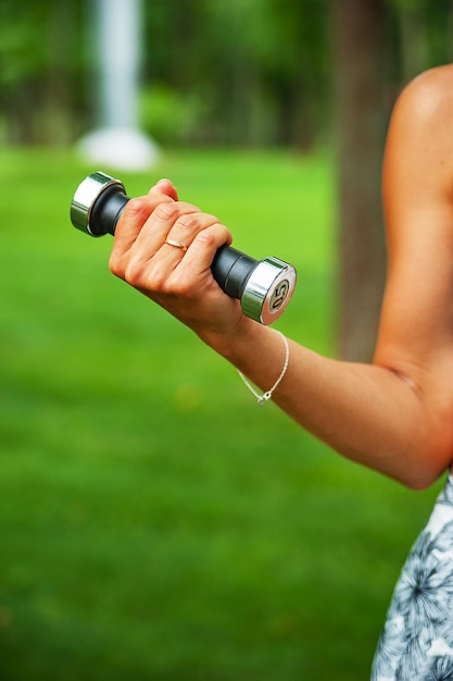 Sports girl holding a dumbbell in her hand at a workout in the park