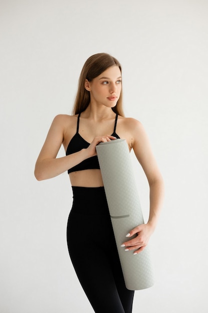 Sports girl holding a fitness mat in her hands on a white background