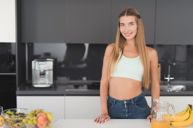 La ragazza di sport sta stando in cucina e sta preparando un'insalata.