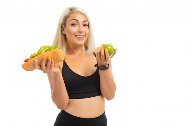 Sports girl in a sports uniform shows an apple and fast food on a camera