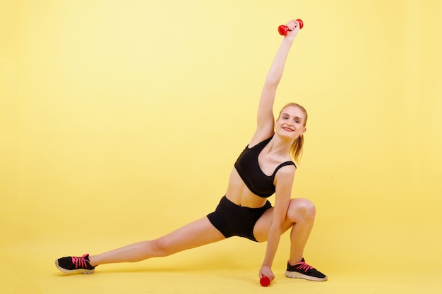 Sports girl trains with dumbbells on a yellow space