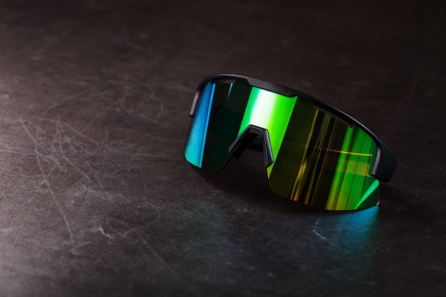 Sports glasses with a green mirrored lens and black frames on a black surface