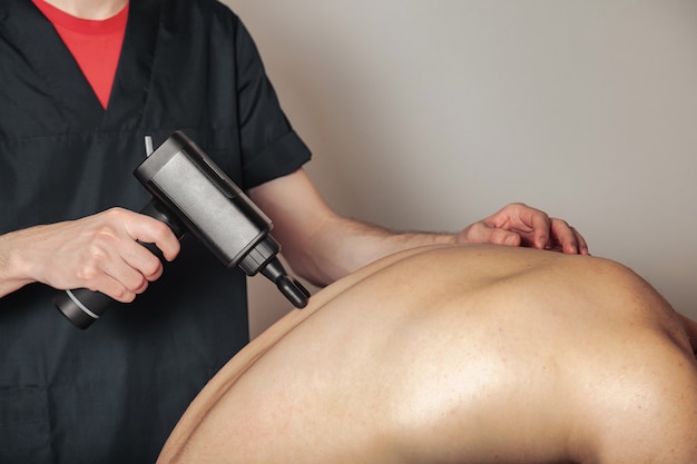 Sports gun percussion massage in medical room of gym. Masseur does home massage exercises 