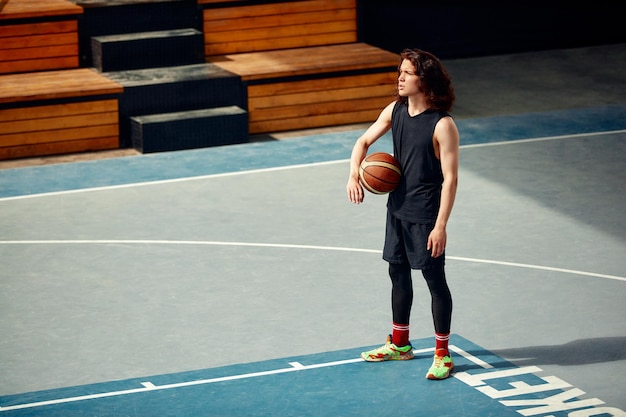 Photo sports guy on the basketball court a guy with long hair trains with the ball on the basketball court