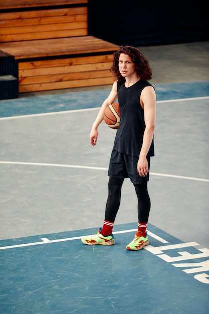 Sports guy on the basketball court a guy with long hair trains with the ball on the basketball court