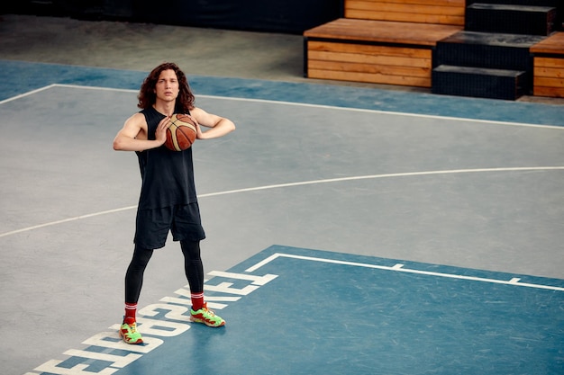 Sports guy on the basketball court a guy with long hair trains with the ball on the basketball court