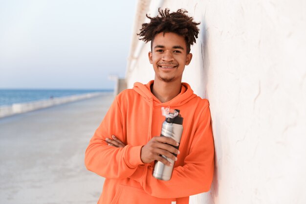 Sports guy outdoors on the beach drinking water holding bottle