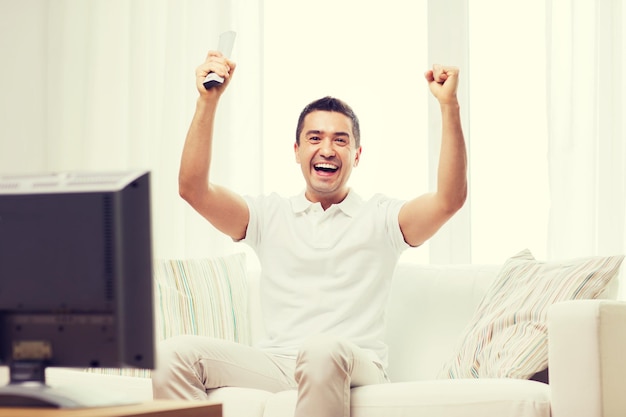 sports, happiness and people concept - smiling man watching sports on tv and supporting team at home