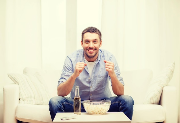 концепция спорта, счастья и людей - улыбающийся мужчина смотрит спорт по телевизору и поддерживает команду дома
