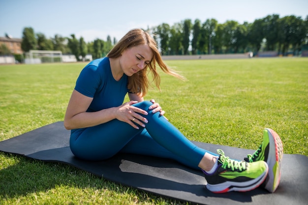 Sports injury of the knee A woman experiences pain in her knee while exercising at a sports stadium healthcare concept