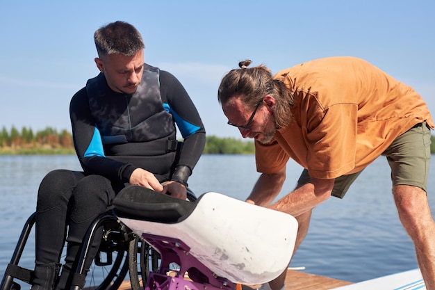 Sports instructor helping man with disability assembling adaptive equipment