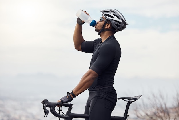 Sports man with a bike drinking water bottle doing fitness training or workout on sky mockup background Healthy professional athlete cyclist with a bicycle during cycling cardio exercise in nature